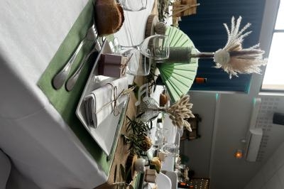 Table décorée pour un repas festif avec nappes blanches, chemins de table verts, vaisselle élégante et décorations…