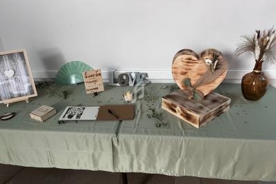 Table décorative avec objets de mariage : cadre, éventail, panneau ’Bienvenue’, cœur en bois, vase et fleurs séchées.