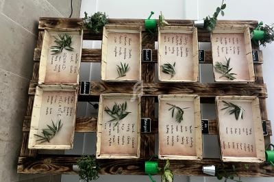 Tableau d'organisation en bois avec des caisses contenant des noms, des feuilles décoratives et des plantes vertes.