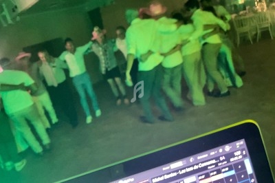 Groupe de personnes dansant en cercle dans une salle faiblement éclairée, vue partielle d'une console de DJ au premier plan.