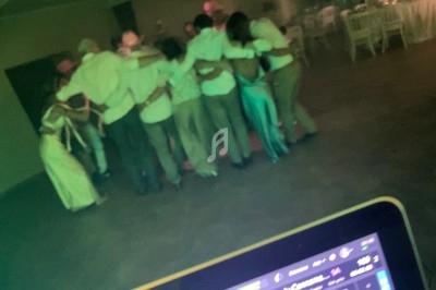 Un groupe de personnes formant un cercle et s'enlaçant dans une salle faiblement éclairée, vue depuis une table de DJ.