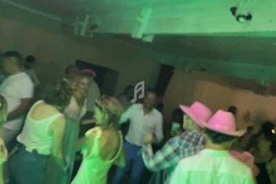 Des personnes dansent dans une salle éclairée par des lumières vertes, certaines portant des chapeaux roses.