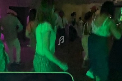 Des personnes dansent dans une salle sombre éclairée par des lumières colorées, avec un écran de mixage en premier plan.