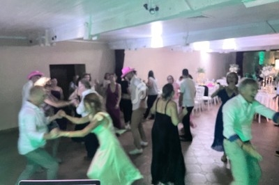 Des personnes dansent en groupe dans une salle éclairée, certaines portant des chapeaux roses.