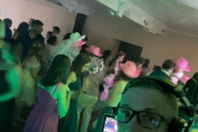 Un DJ avec casque anime une soirée dansante dans une salle éclairée par des lumières colorées, avec des invités en arrière…