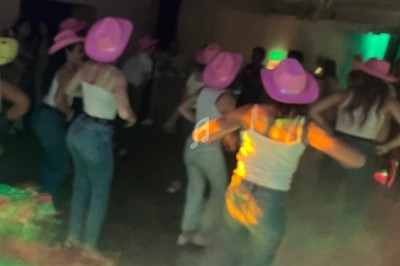 Des personnes dansant en groupe, portant des chapeaux roses et des tenues décontractées, dans une salle éclairée.