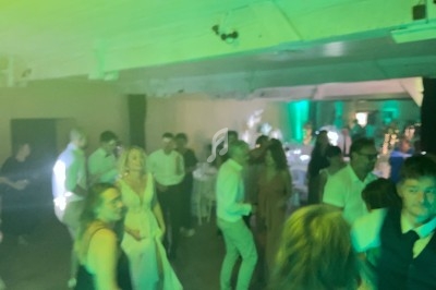 Personnes dansant dans une salle éclairée par des lumières vertes, avec des tables dressées en arrière-plan.