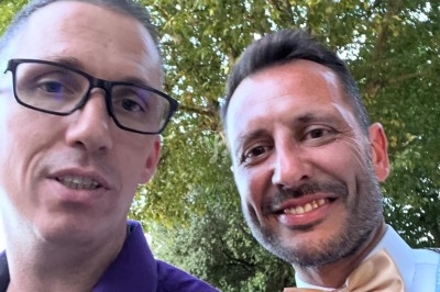 Deux hommes souriants posent en extérieur devant des arbres, l'un porte une chemise violette, l'autre un nœud papillon doré.
