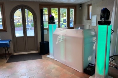 Poste de DJ avec une table recouverte de tissu blanc et deux colonnes lumineuses vertes dans une salle lumineuse.