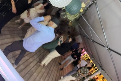 Personnes dansant sous une tente éclairée, avec des décorations suspendues et un sol en bois.