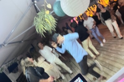 Des personnes dansent sous une tente éclairée, avec des décorations suspendues et un sol en bois.