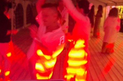 Personnes dansant sous une tente éclairée par des lumières rouges, avec un DJ en arrière-plan.