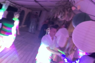 Des personnes dansent sous une tente éclairée par des lumières colorées lors d'une soirée festive.