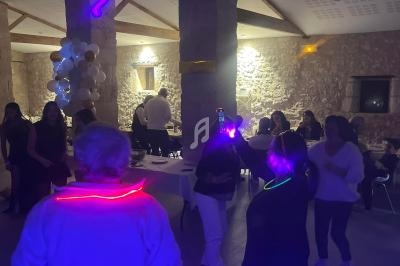 Des personnes dansent dans une salle en pierre éclairée par des lumières colorées et des décorations festives.