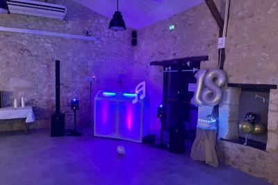 Salle en pierre décorée pour une fête avec une table de mixage lumineuse, ballons ’18’ et éclairage coloré.
