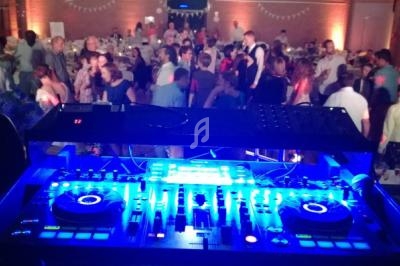 Vue depuis une table de mixage éclairée en bleu, face à une salle remplie de personnes lors d'un événement festif.