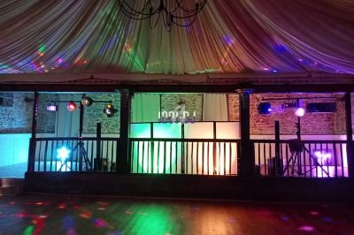 Salle de réception avec éclairages colorés, piste de danse en bois et plafond drapé.