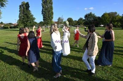Un groupe de personnes forme une ronde autour d'une mariée tenant un bouquet, dans un parc ensoleillé.