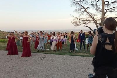 Un groupe de personnes dansant en plein air au coucher du soleil, photographié par une femme de dos.