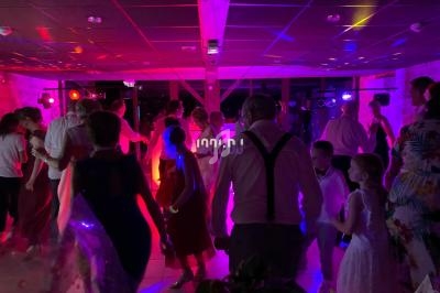 Des personnes dansent dans une salle éclairée par des lumières colorées lors d'une fête ou d'un événement festif.
