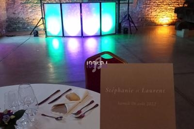 Salle de réception éclairée avec piste de danse, table dressée au premier plan et menu mentionnant un mariage.