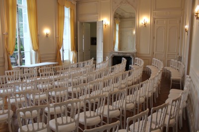 Façade d'un château illuminé la nuit avec une fontaine ornée de statues au premier plan.