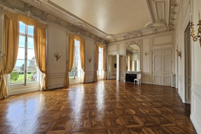 Façade d'un château illuminé la nuit avec une fontaine ornée de statues au premier plan.