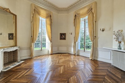 Façade d'un château illuminé la nuit avec une fontaine ornée de statues au premier plan.