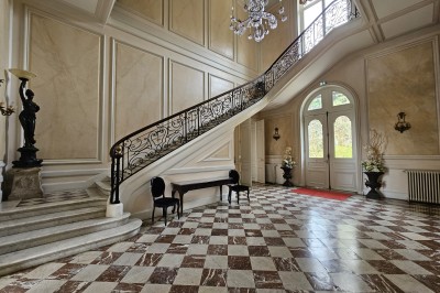 Façade d'un château illuminé la nuit avec une fontaine ornée de statues au premier plan.