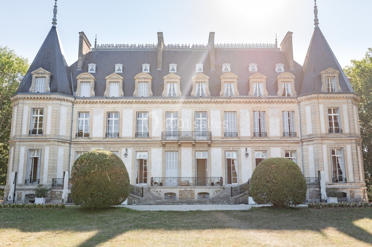 Façade d'un château de style classique avec toits en ardoise, entouré de pelouse et de buissons taillés.