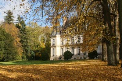 Façade d'un château illuminé la nuit avec une fontaine ornée de statues au premier plan.