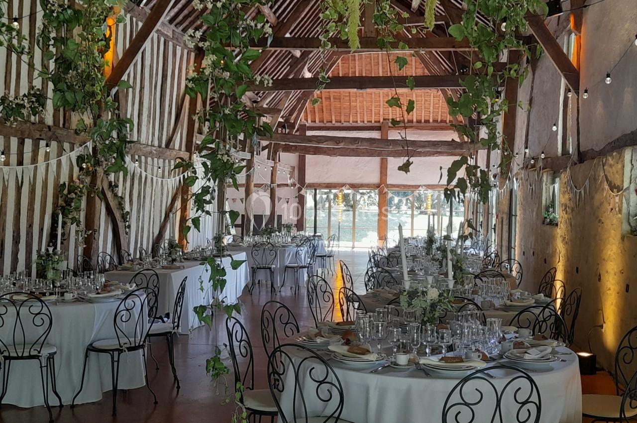 Salle de réception décorée avec des tables rondes dressées, des chaises en fer forgé et des guirlandes de feuillage…
