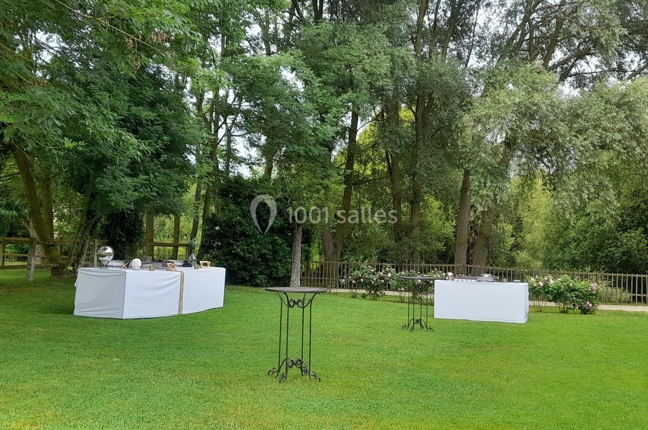 Tables de buffet dressées sur une pelouse verte entourée d'arbres dans un cadre extérieur paisible.