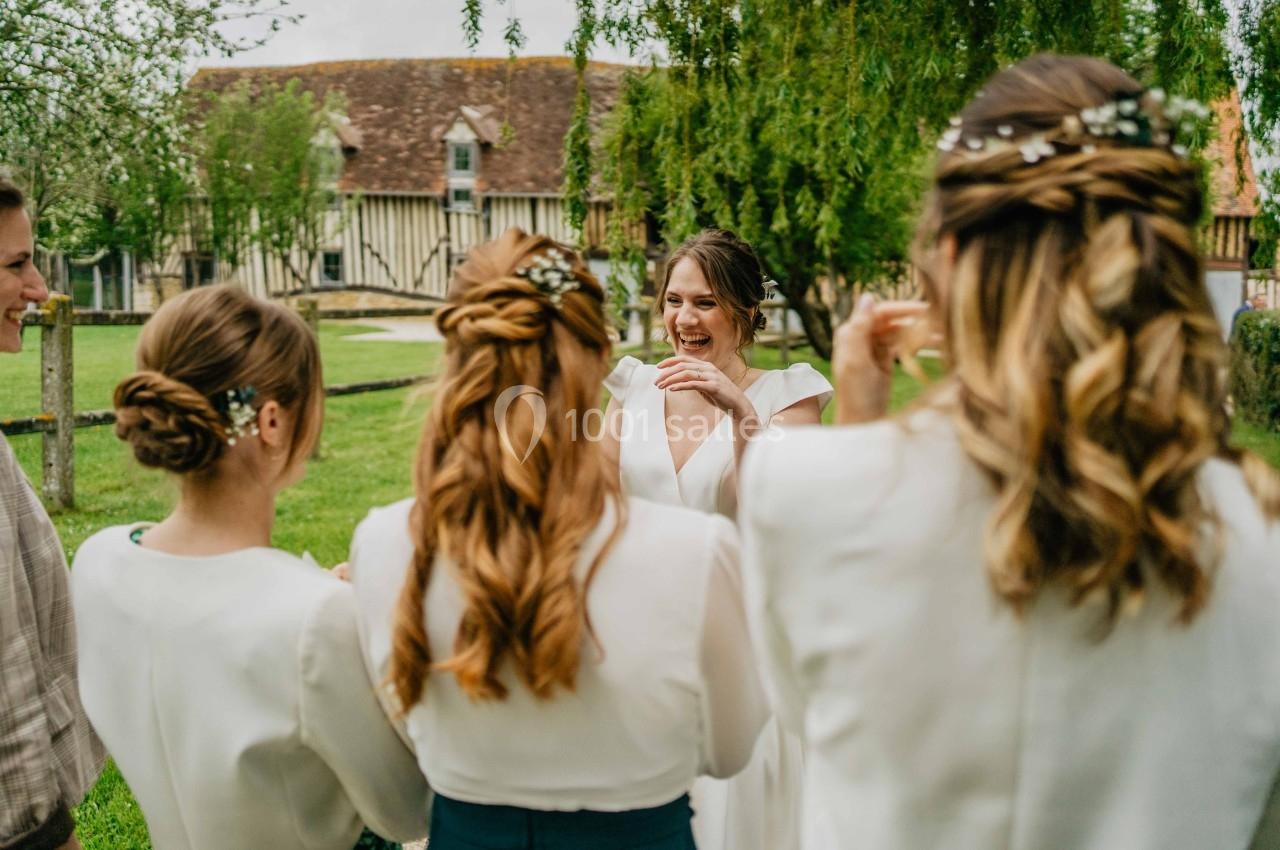 Une mariée souriante entourée de ses demoiselles d'honneur dans un jardin verdoyant devant une maison à colombages.