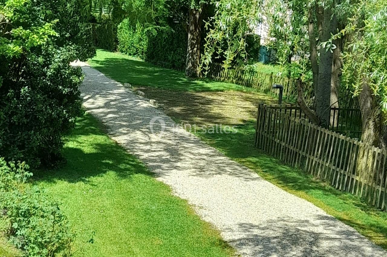 Chemin de gravier bordé de pelouse et d'arbres, menant à une clôture en bois dans un cadre verdoyant.