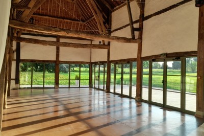 Salle de réception rustique avec tables rondes dressées, chaises en fer forgé et drapés blancs suspendus au plafond.