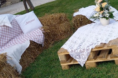 Salle de réception rustique avec tables rondes dressées, chaises en fer forgé et drapés blancs suspendus au plafond.