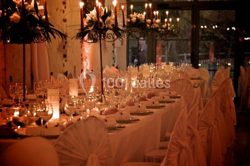 Salle de réception élégamment décorée avec des tables dressées, des chandeliers et une lumière tamisée.