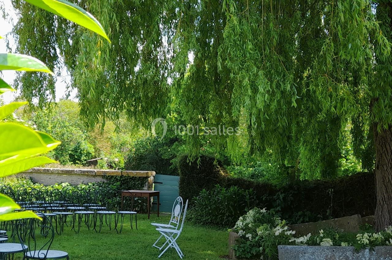 Chaises blanches et noires disposées dans un jardin ombragé sous un grand saule pleureur.
