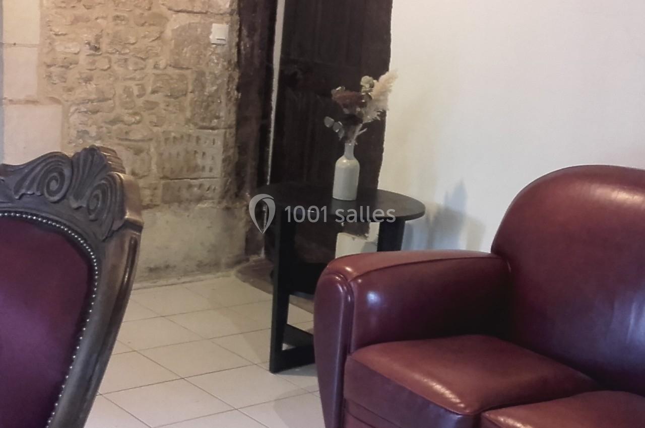 Un fauteuil en cuir rouge près d'une table noire avec un vase de fleurs, dans une pièce aux murs en pierre.