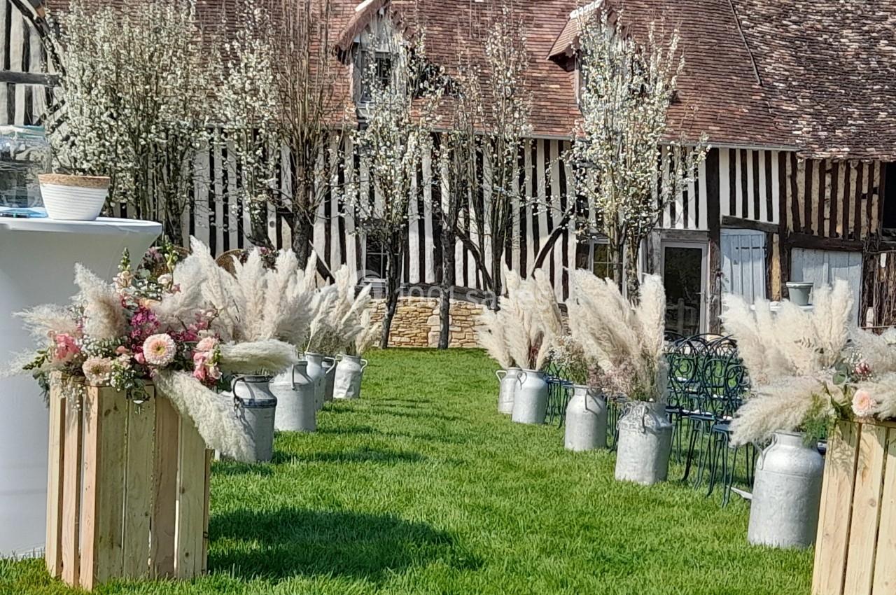 Allée décorée de fleurs séchées et d'herbes de la pampa, devant une maison à colombages et des arbres en fleurs.