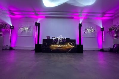 Console de DJ illuminée avec des projecteurs roses dans une salle décorée de fleurs blanches.