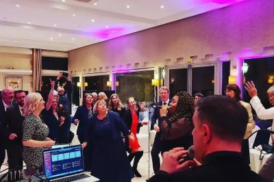 Des personnes dansent et chantent dans une salle éclairée de lumières colorées, avec un chanteur au premier plan.