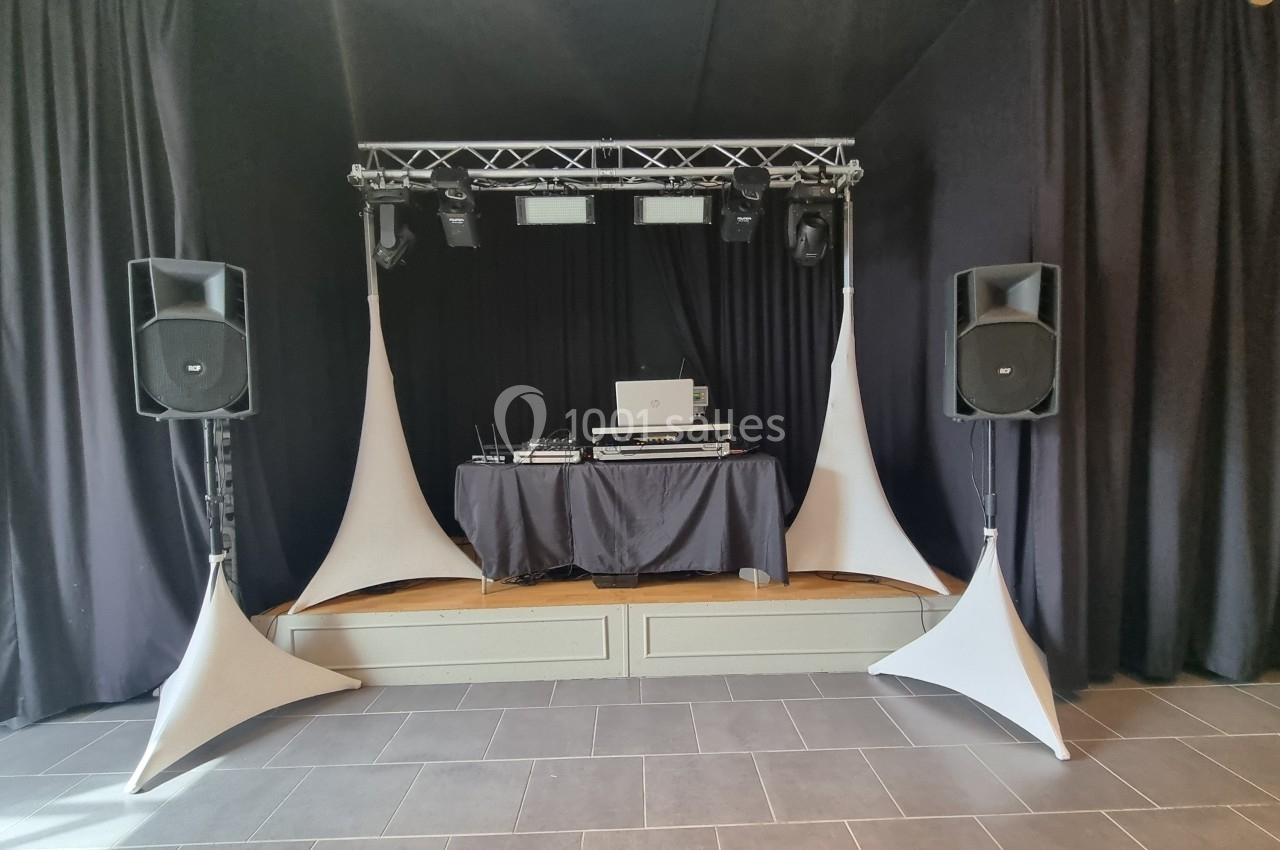 Scène avec équipement de DJ comprenant une table de mixage, des enceintes et des éclairages, entourée de rideaux noirs.