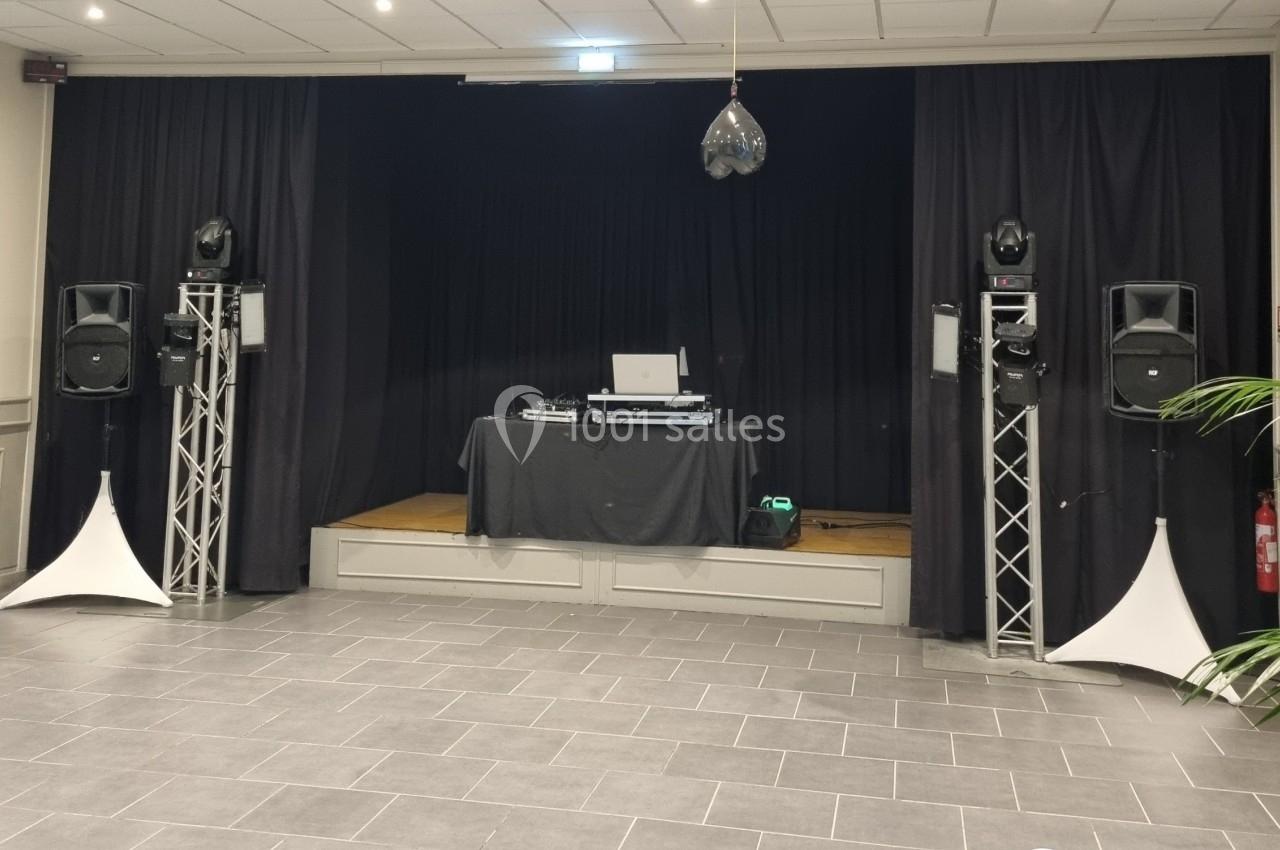 Scène avec table de mixage, ordinateur portable, enceintes sur pieds et rideaux noirs en arrière-plan.