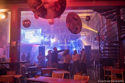 Deux DJ mixent sur une scène éclairée par des projecteurs colorés, devant un écran affichant ’Don't Care Project’.