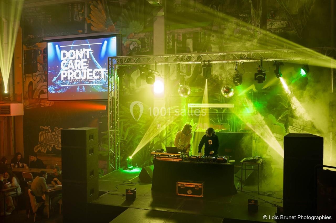 Deux DJ mixent sur une scène éclairée par des projecteurs colorés, devant un écran affichant ’Don't Care Project’.