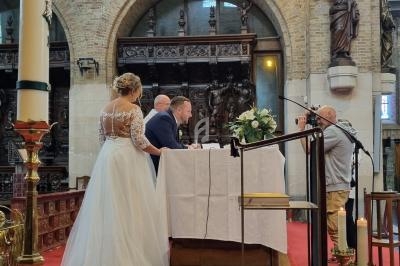 Un couple se tient devant un autel dans une église lors d'une cérémonie, avec un photographe à droite.