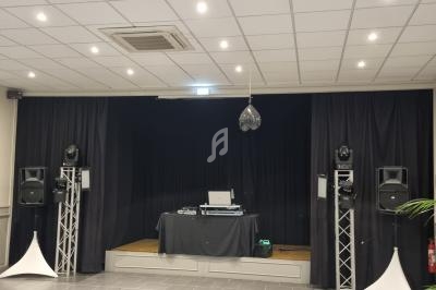 Scène avec rideaux noirs, table de mixage, enceintes sur pieds et éclairage suspendu dans une salle moderne.
