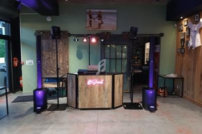 Console de DJ en bois avec éclairage rose, entourée de haut-parleurs et de projecteurs dans une salle moderne.